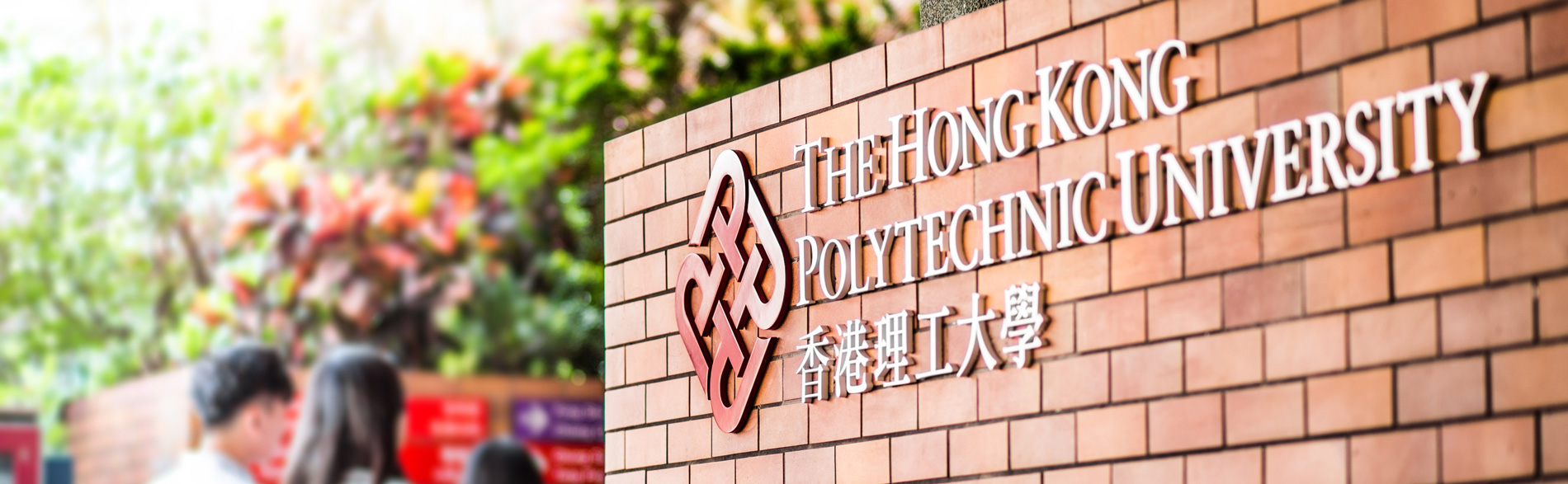 The Hong Kong Polytechnic University sign on brick wall with students entering.