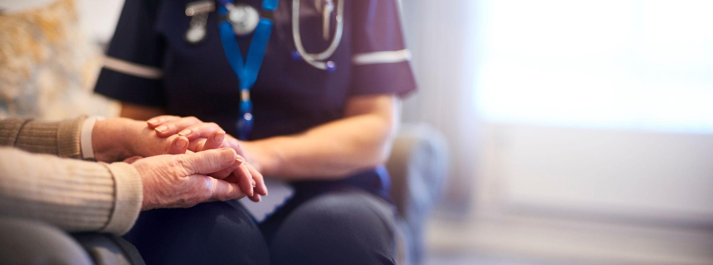 Nursing student sits with aged care resident holding hands