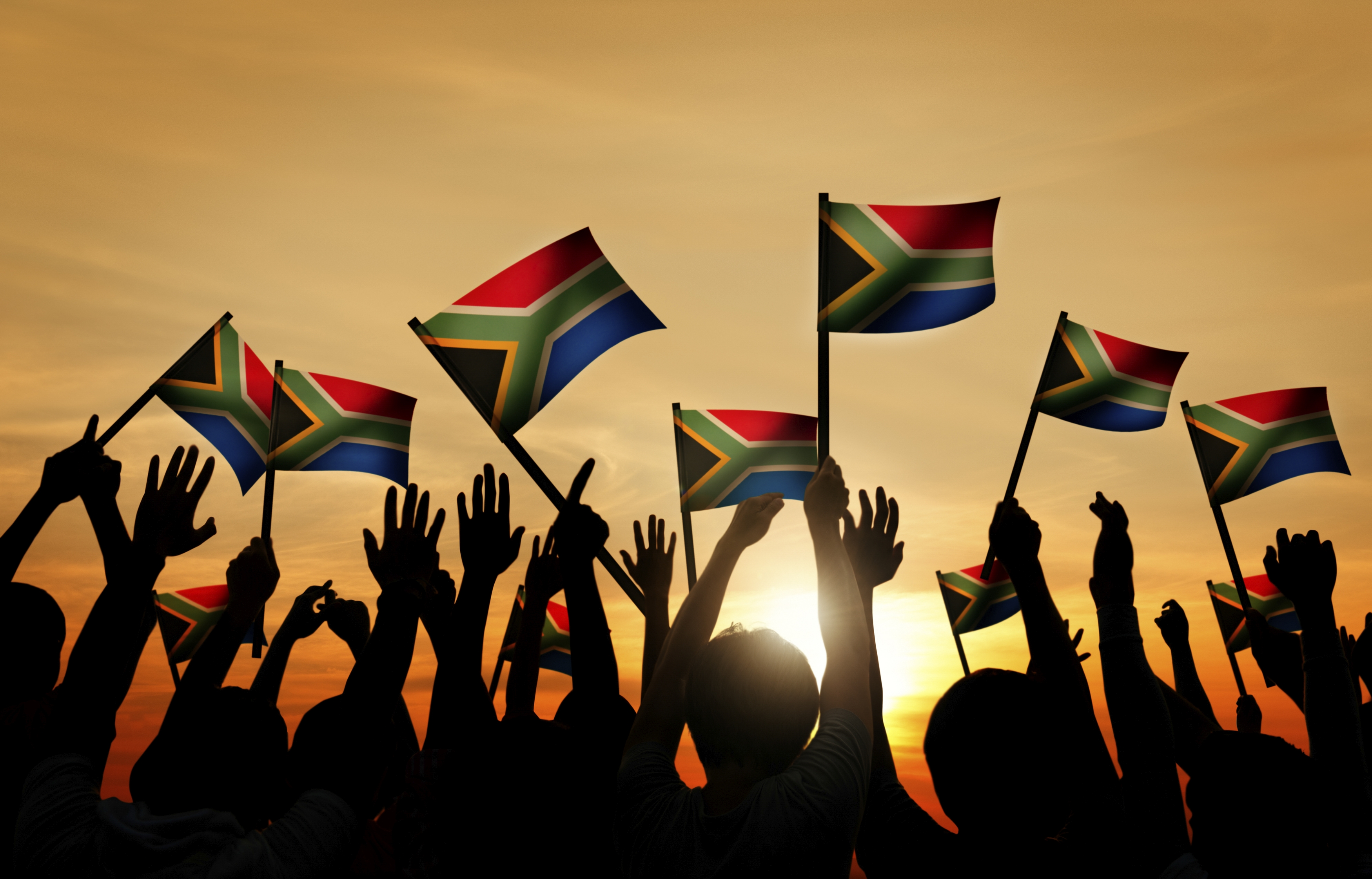 A group of silhouettes holding up South African flags as the sun sets 