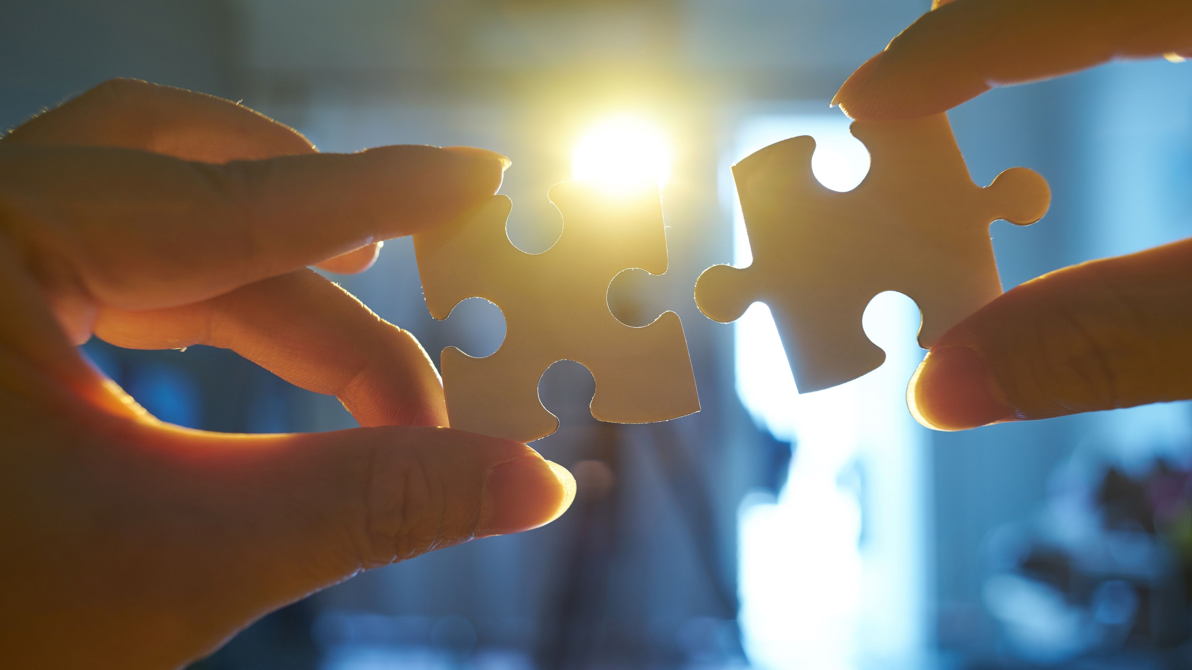 Two hands holding separate jigsaw pieces move together with light in background
