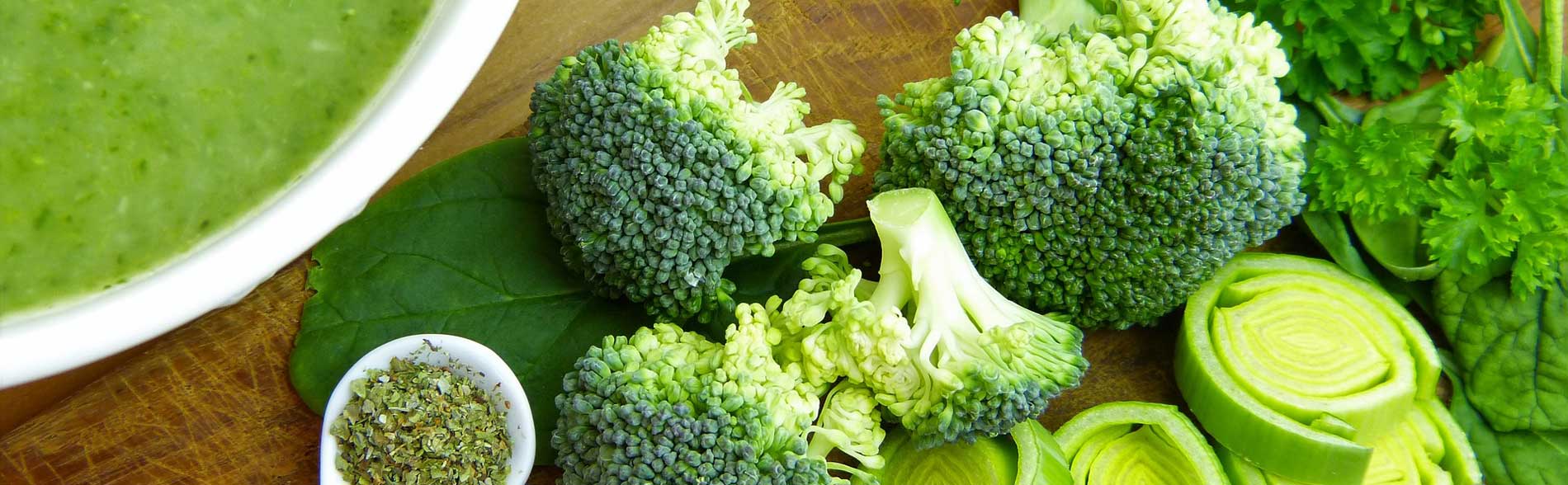 Close up of nutritious green foods like green vegetable soup, broccoli florets, herbs, spinach