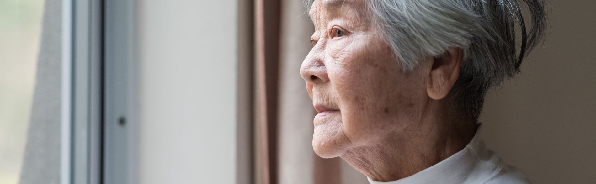 Woman separated from her spouse in long term care looks out a window