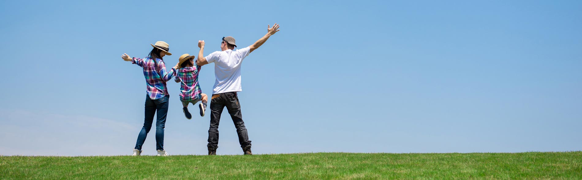 Two parents swing their child in the air on a grassy hill