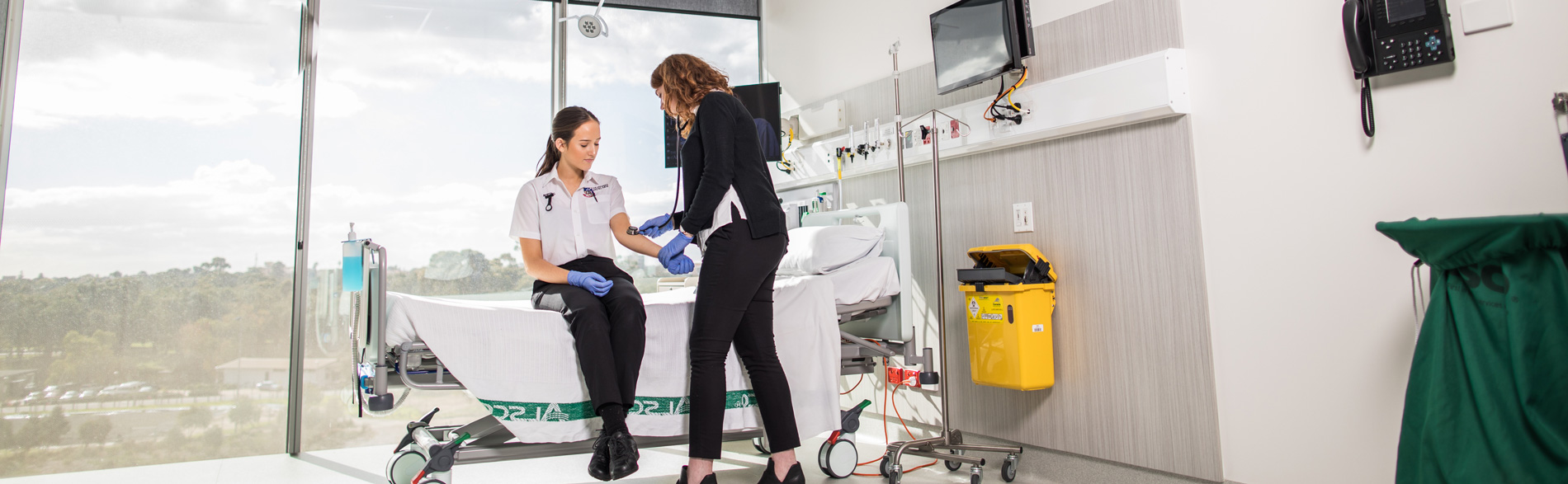 Adelaide University nursing student sits on a hospical bed receiving training from another clinician