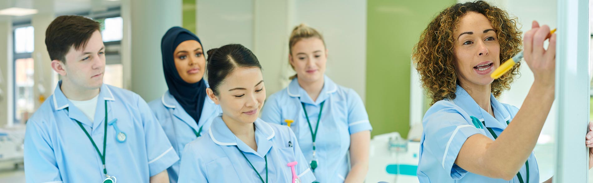 A group of nursing students in a team meeting with leader who is writing on a whiteboard