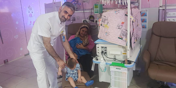 Doctor holds child while mother looks on with baby.