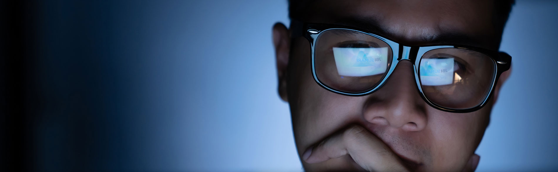 Man working on a laptop with screen reflected in his glasses