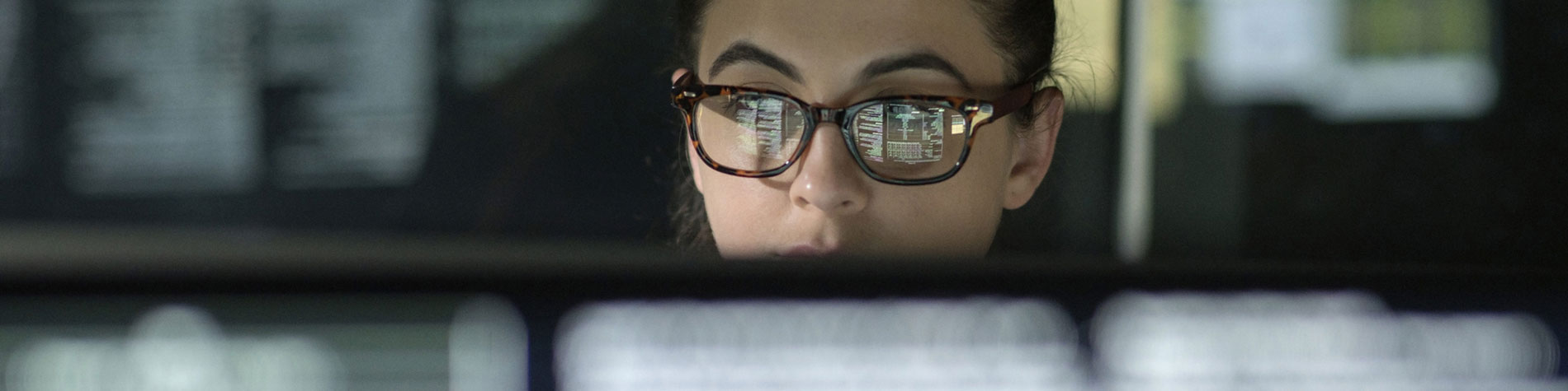 A close up of a woman with a computer screen reflected in her glasses