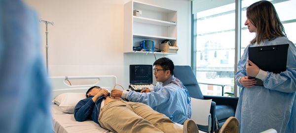 A student nurse is supervised while examining another student nurse in a clinical setting