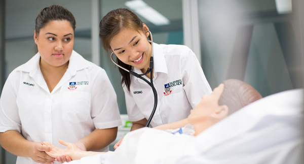 Two student nurses examine a practice dummy.