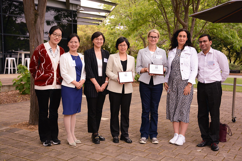 Members of the JBI Collaboration Entities celebrating their anniversaries pose together for a group shot with their 10 year anniversary and 20 year anniversary plaques