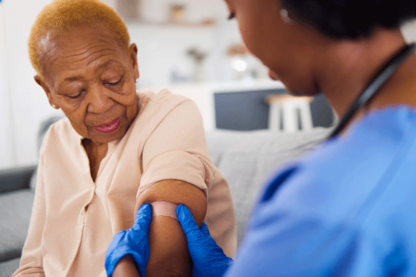 Female clinician applying a bandaid on the arm of her female patient following a Pneumococcal vaccination
