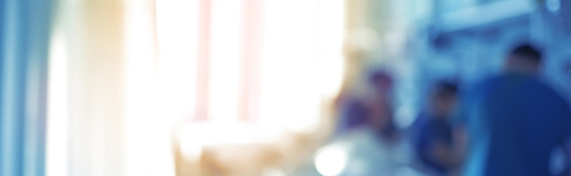 Blurred image of clinicians working around a hospital bed.