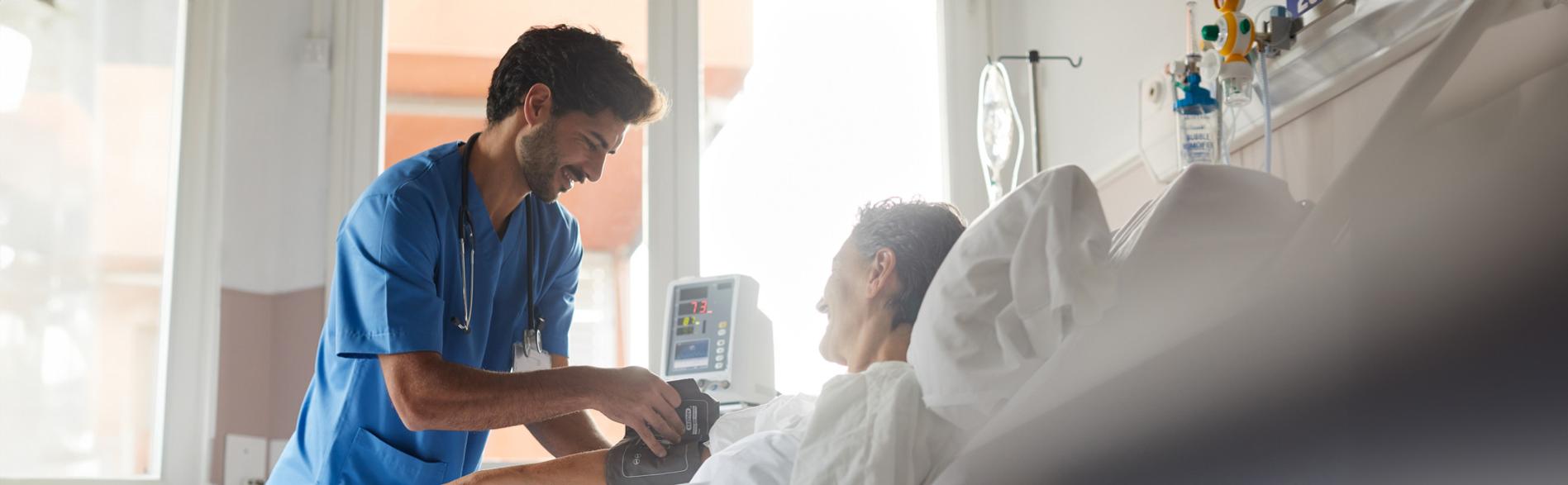 A clinician takes the blood pressure of a patient in a hospital bed